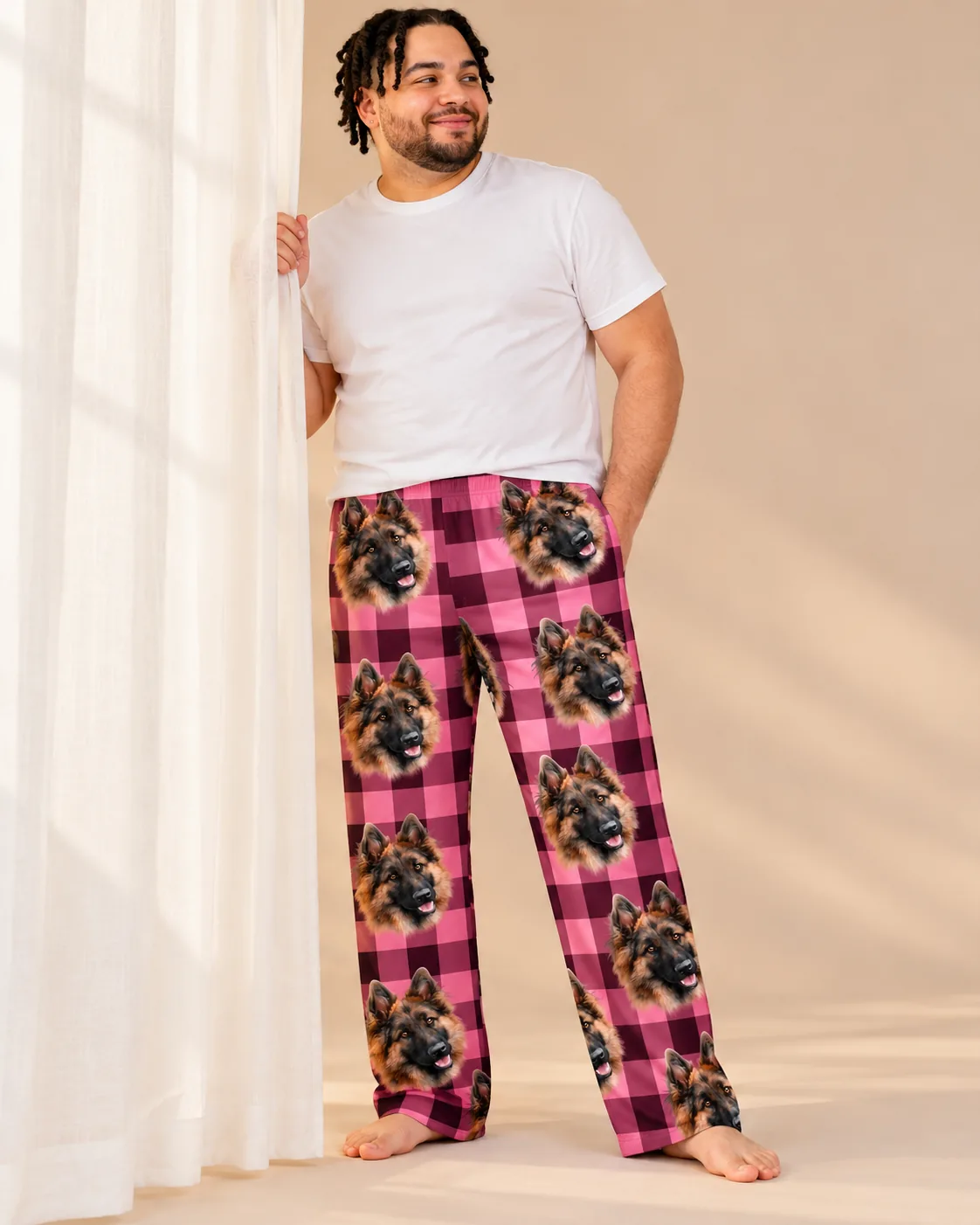 Man by a sheer curtain in pink plaid pajama pants with German Shepherd faces on a warm beige backdrop