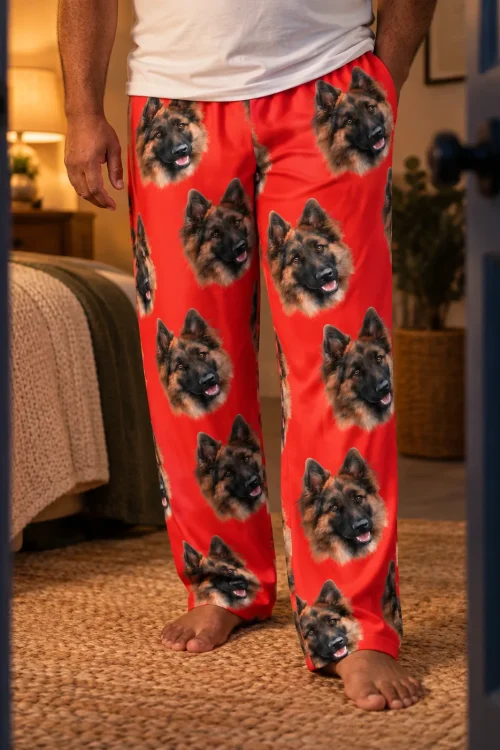 Close view of red pajama pants with German Shepherd faces on a barefoot man in a cozy bedroom doorway