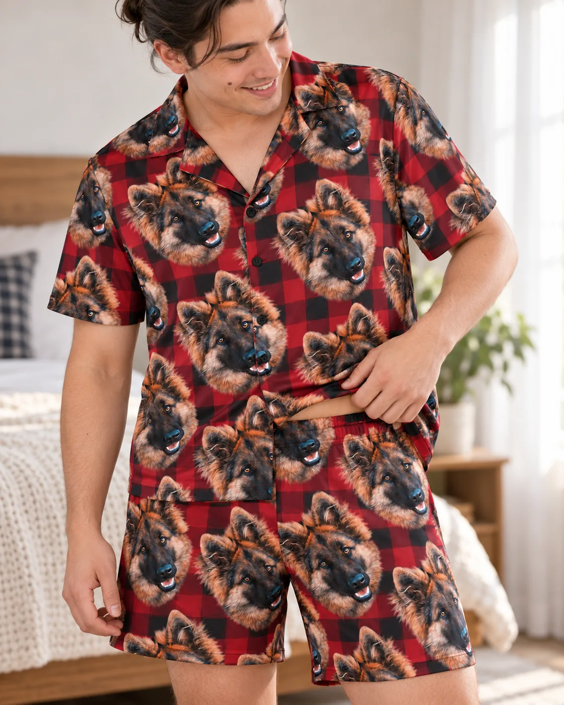 Man adjusting his red and black plaid pajama shirt with German shepherd faces in a bright bedroom