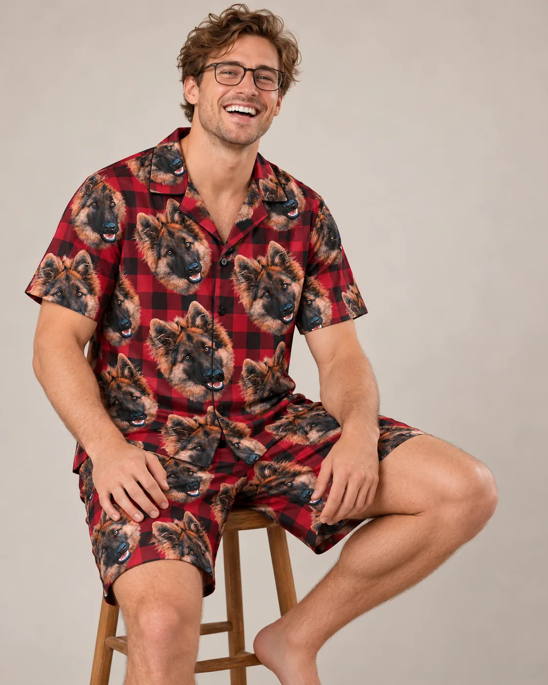 Laughing man on a wooden stool in red plaid pajamas, shirt and shorts with German shepherd faces