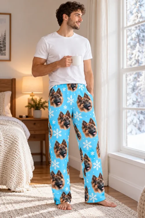 Man in sky blue snowflake pajama pants with German Shepherd faces holding a mug by a snowy window