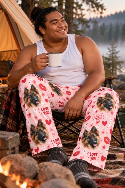 Man with an enamel mug at a lakeside campsite in pink Valentine pajama pants with German Shepherd faces