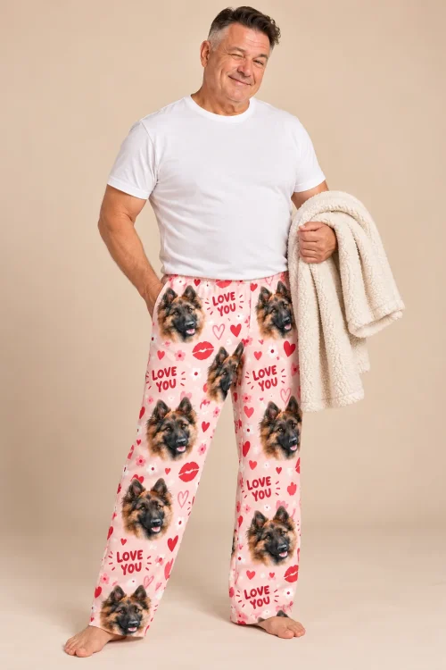 Man in pink Valentine pajama pants with German Shepherd faces and Love You hearts on a beige backdrop