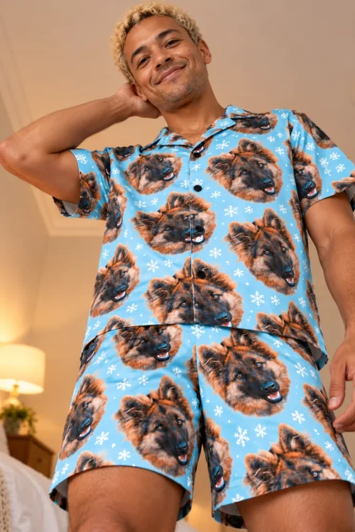 Smiling man in a light blue snowflake pajama shirt and shorts with German shepherd faces