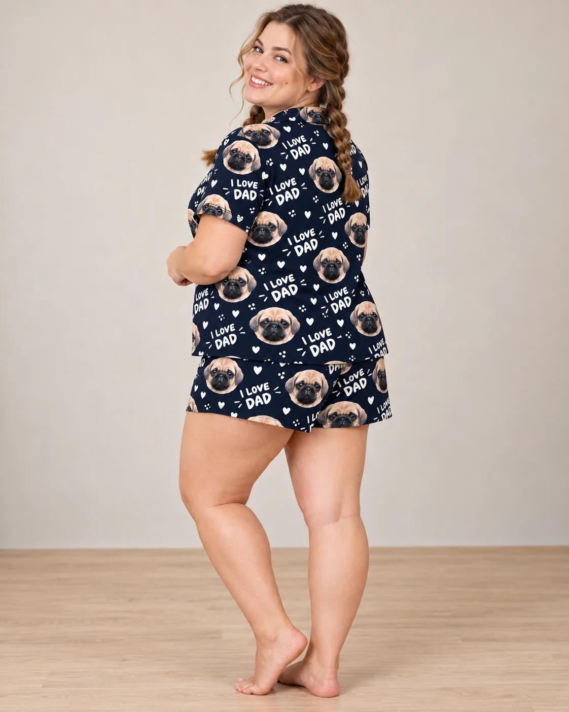 Smiling woman with braids looks back in a navy I Love Dad short pajama set with fawn pug faces and hearts, studio