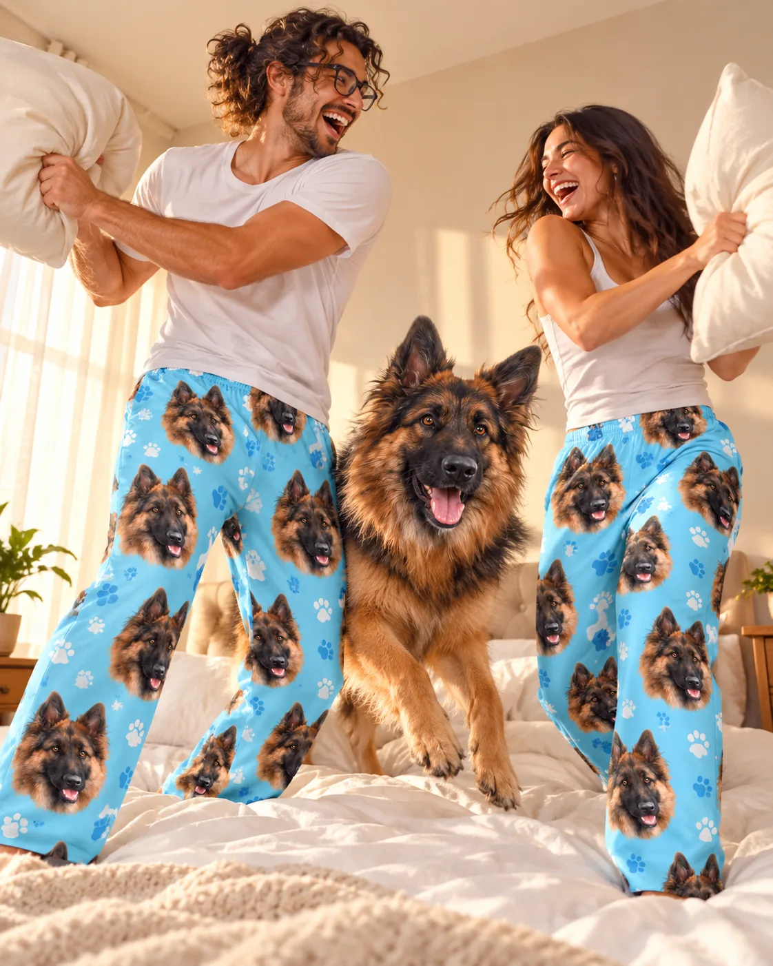 Couple has a pillow fight on the bed with their German shepherd, both in light blue paws pajama pants