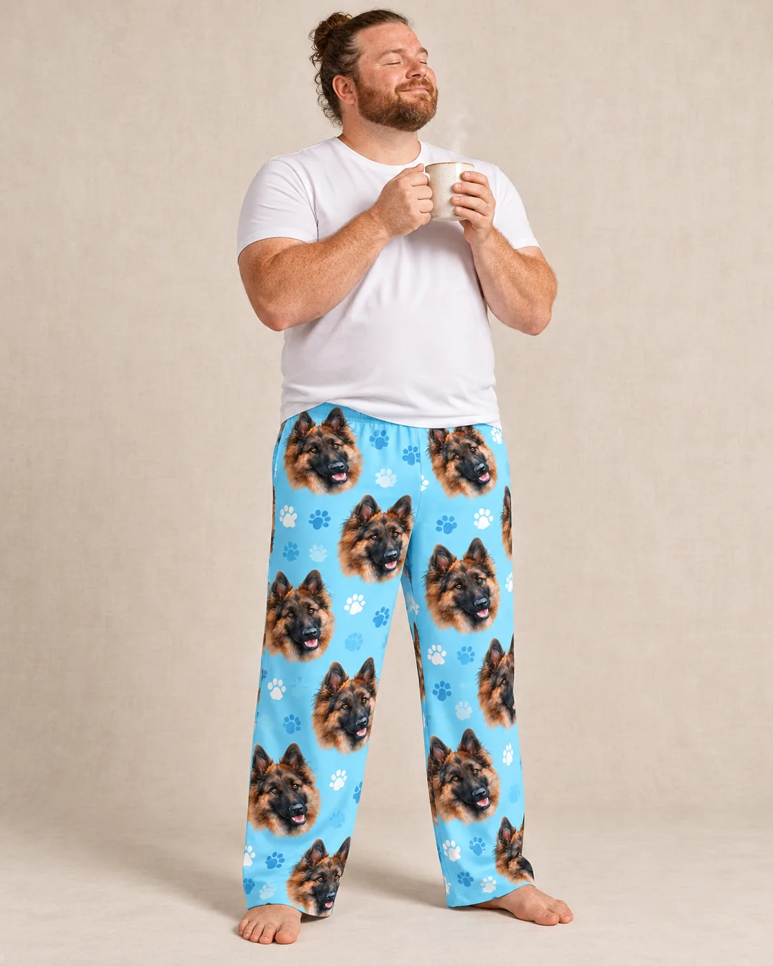 Man sips coffee in a studio in light blue paws pajama pants printed with German shepherd faces
