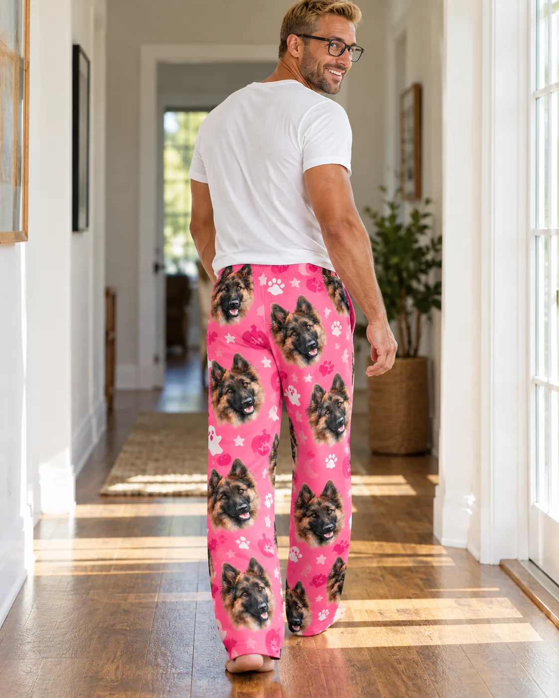 Man in glasses walks down a sunny hallway in pink German shepherd face pajama pants