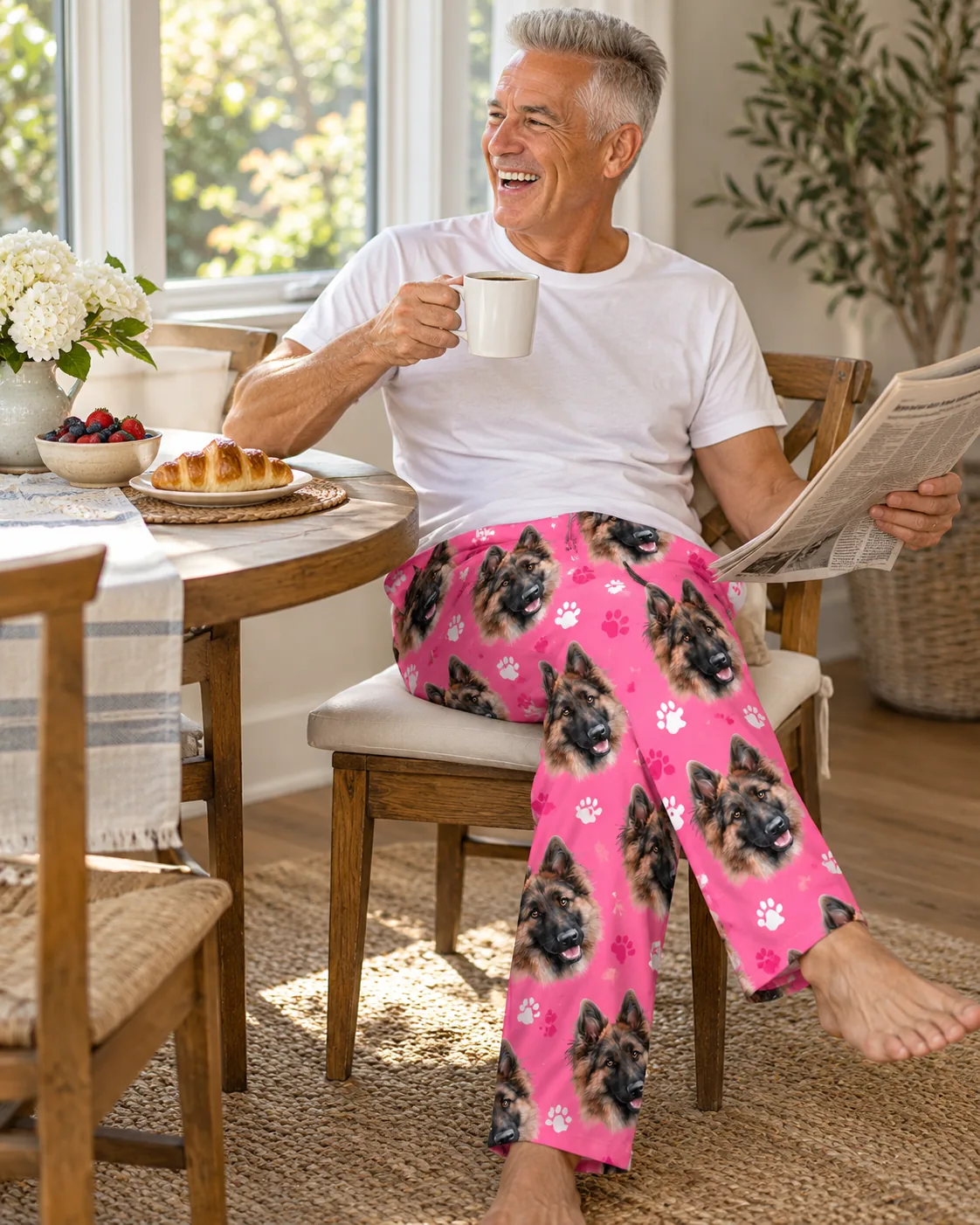 Smiling man with coffee and a newspaper at breakfast in pink paws German shepherd face pajama pants