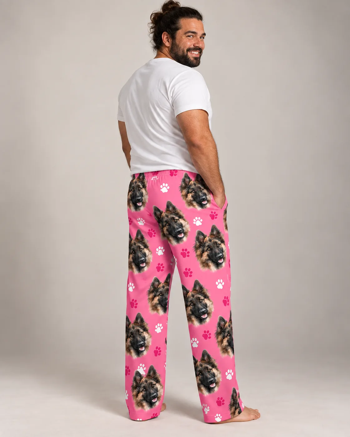 Bearded man in a white tee looks back over his shoulder in pink paws pajama pants with German shepherd faces