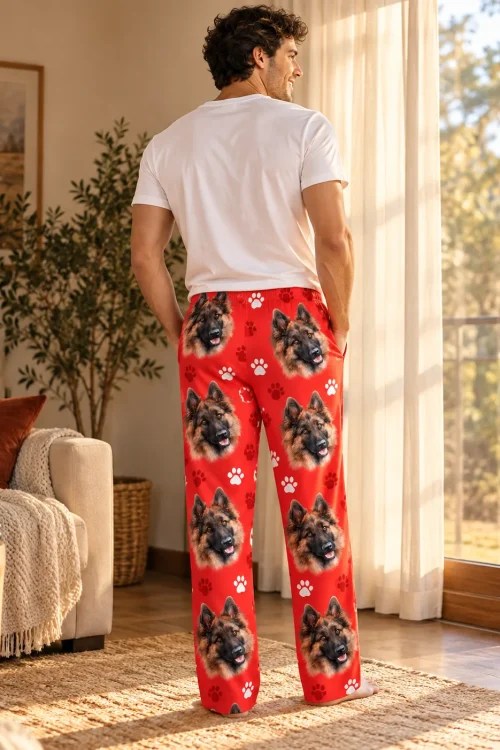 Man gazes out a sunlit window, back view of red paws pajama pants with German shepherd faces
