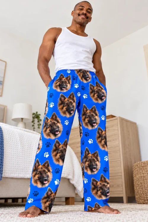 Man in a white tank stands in a bedroom in royal blue paws pajama pants with German shepherd faces