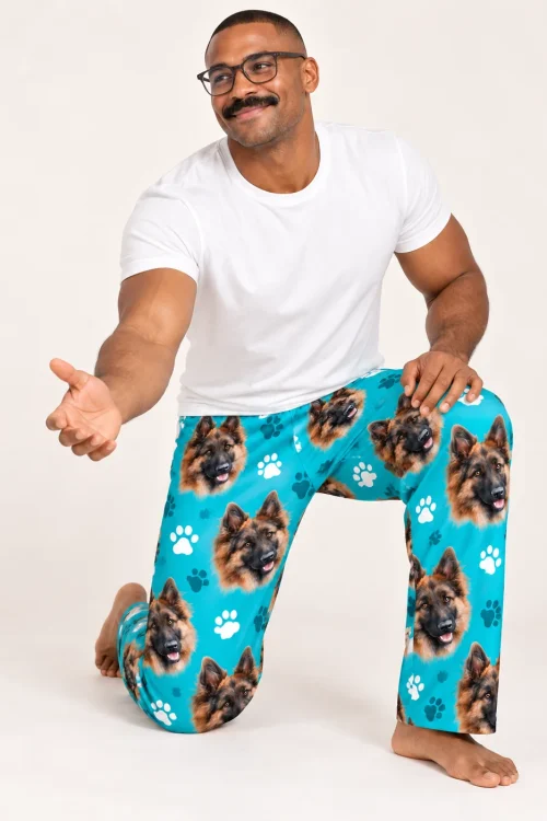 Kneeling man in glasses reaches out in teal paws pajama pants printed with German shepherd faces