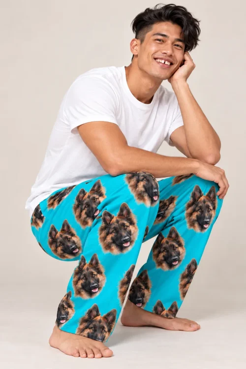 Smiling man crouches in a studio in teal pajama pants printed with German shepherd faces