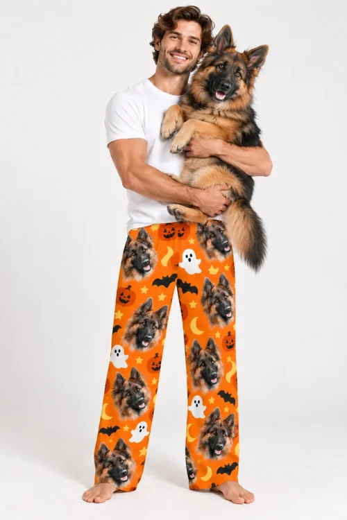 Man holding his German shepherd in pet face pajama pants with a Halloween print
