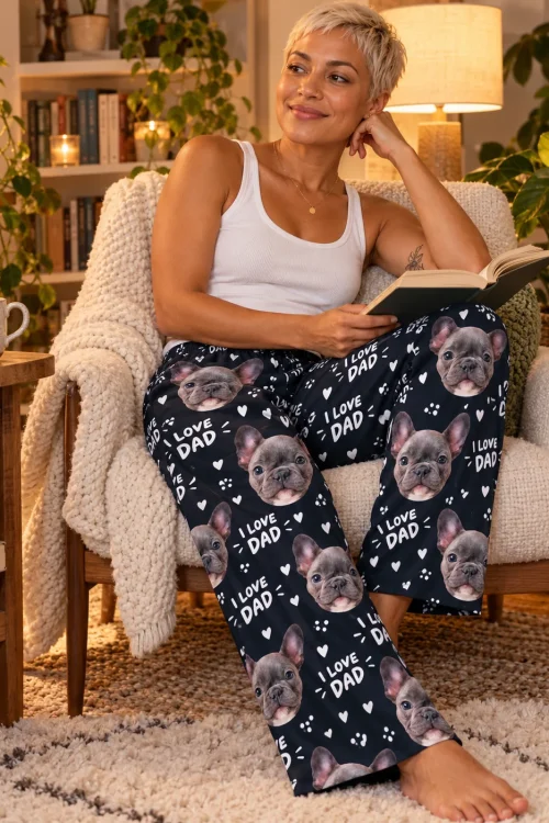 Woman reading in a cozy armchair wearing navy I Love Dad pajama pants printed with grey French bulldog faces