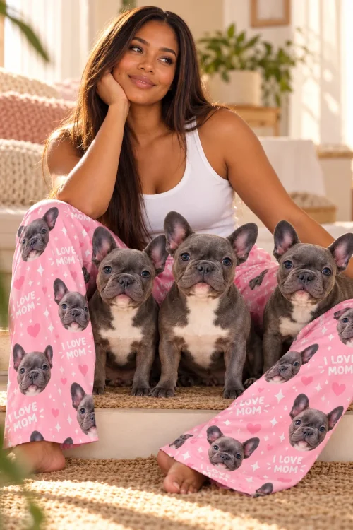 Smiling woman sits on sunny steps with three grey French bulldogs, wearing pink I Love Mom French bulldog pajama pants