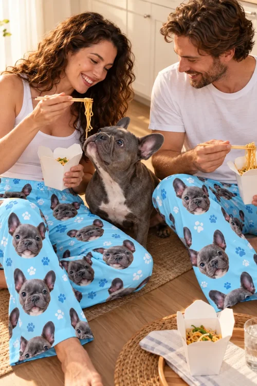 Couple eating noodles on the floor in light blue paw print French bulldog pajama pants as their grey Frenchie begs