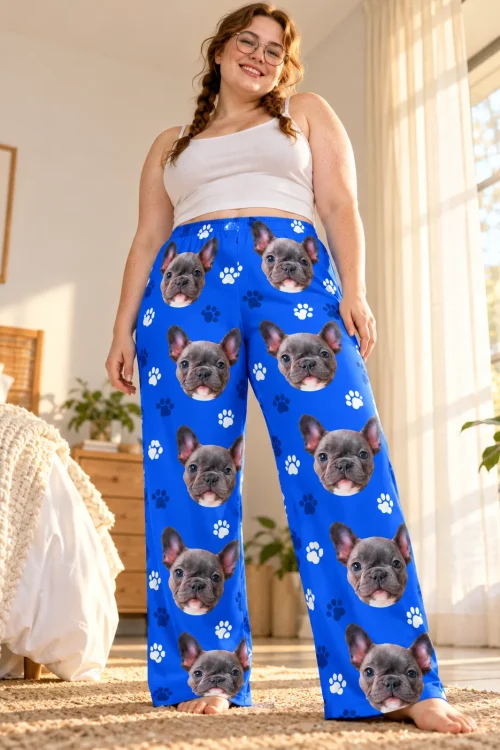 Smiling woman with braids and glasses in a sunny bedroom wearing royal blue paw print French bulldog pajama pants