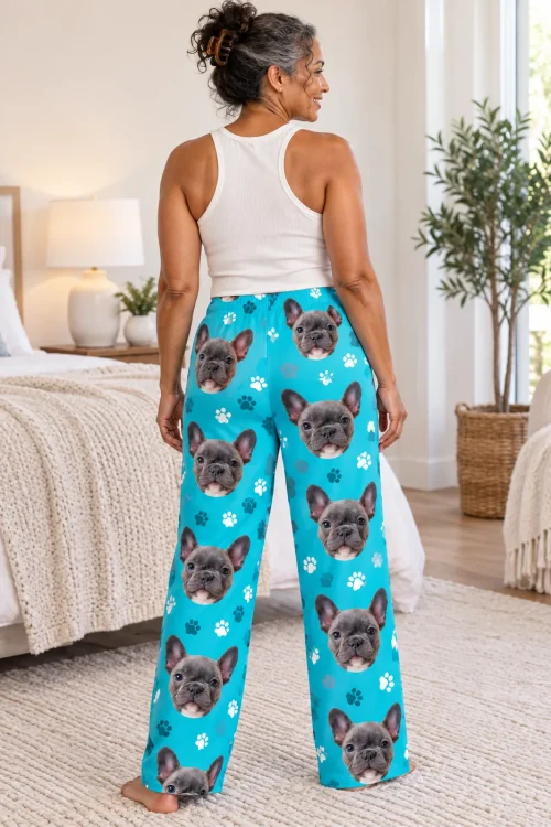Back view of woman in a bright bedroom wearing teal paw print pajama pants printed with grey French bulldog faces