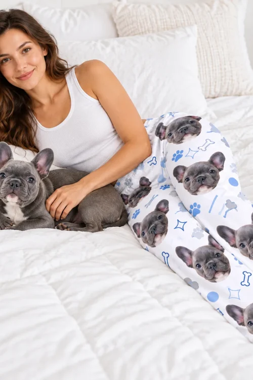 Woman lounging on a bed with her French bulldog, wearing pet face pajama pants of the same dog