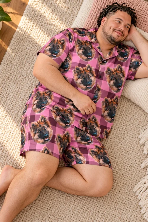 Smiling man lying on a cozy rug with pillows in a pink plaid short pajama set printed with German shepherd faces