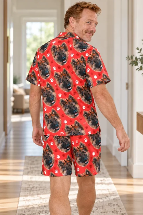 Back view of smiling man in a sunny hallway in a red paw print short pajama set printed with German shepherd faces
