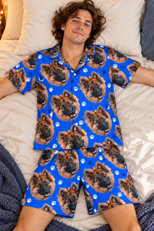 Smiling man lying on a white bed in a royal blue paw print short pajama set printed with German shepherd faces