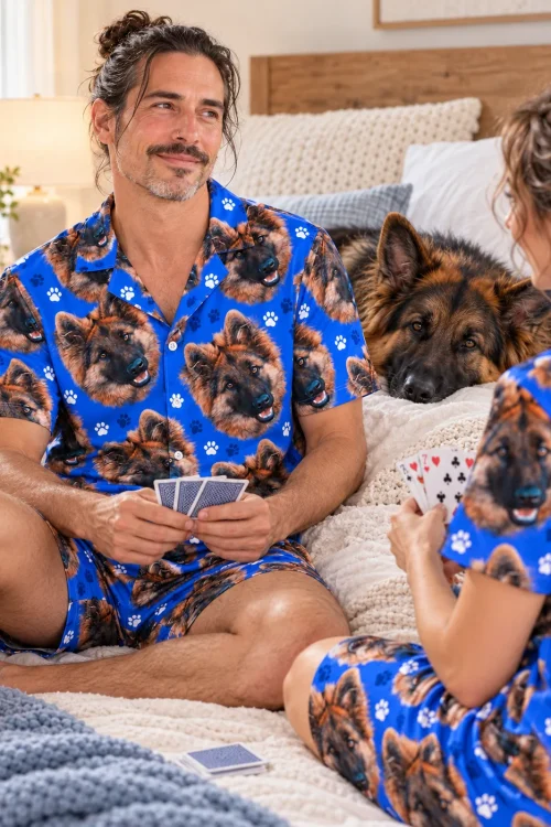 Couple playing cards on a bed in royal blue paw print German shepherd pajama sets as their German shepherd looks on