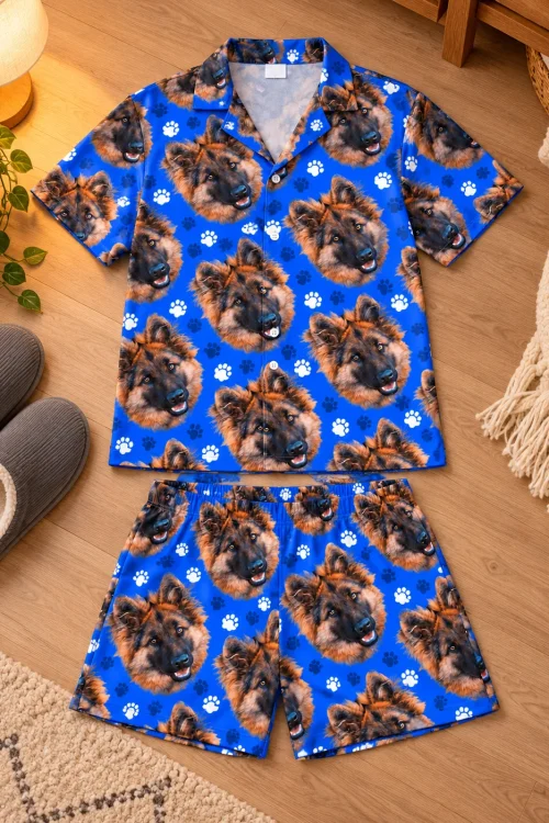 Royal blue paw print short pajama set with German shepherd faces laid flat on a wood floor beside grey slippers