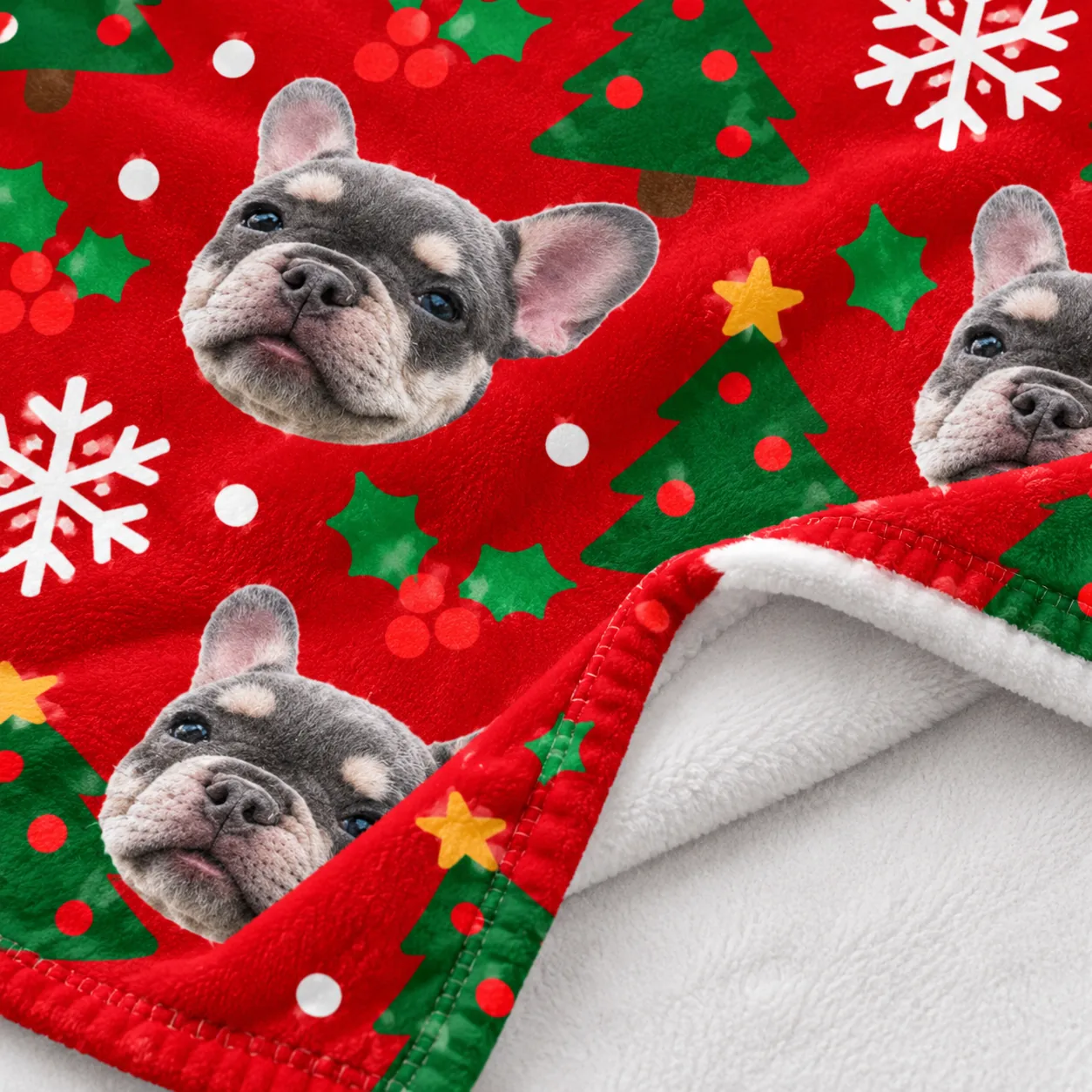 Close-up of a red Christmas fleece blanket printed with a French bulldog's cut-out face, snowflakes and trees