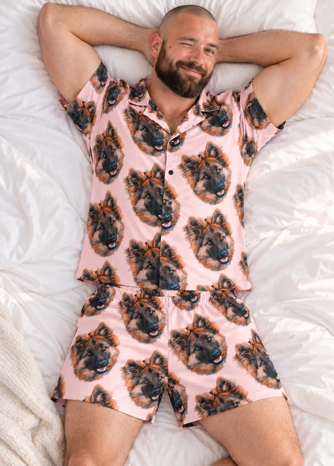 Bearded man winking on white bedding in pale pink pajamas with German shepherd faces