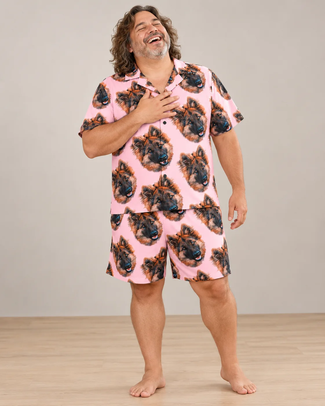 Laughing man with long curly hair in light pink pajamas printed with German shepherd faces
