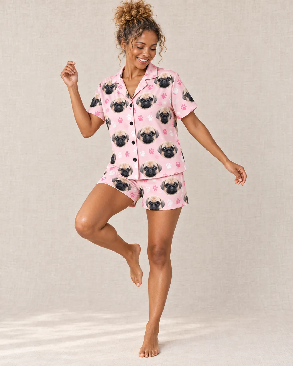 Pink pajamas: woman dancing in a blush pink paw-print short set printed with pug faces