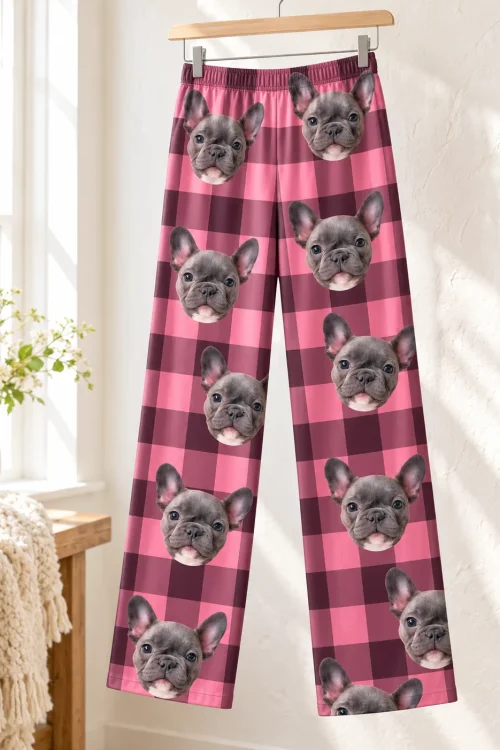 Pink plaid pajama pants with French bulldog faces on a wooden hanger in a bright room