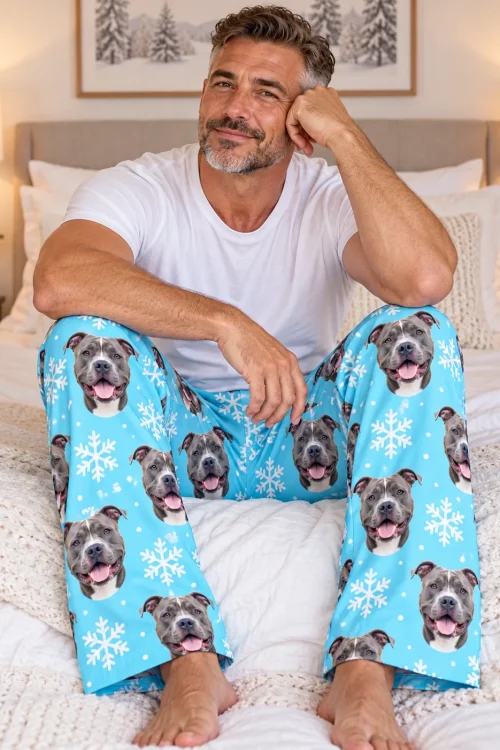 Man sitting cross-legged on a white bed in light blue snowflake pitbull pajama pants