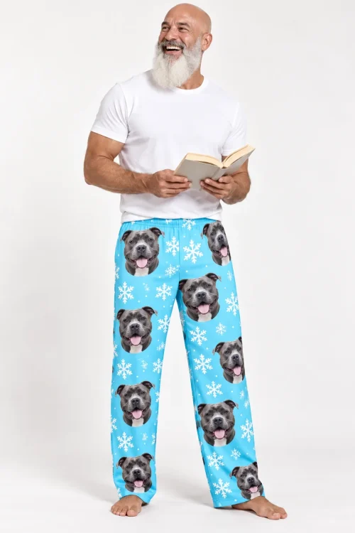 Bearded man laughing with a book in light blue snowflake pitbull pajama pants in a white studio