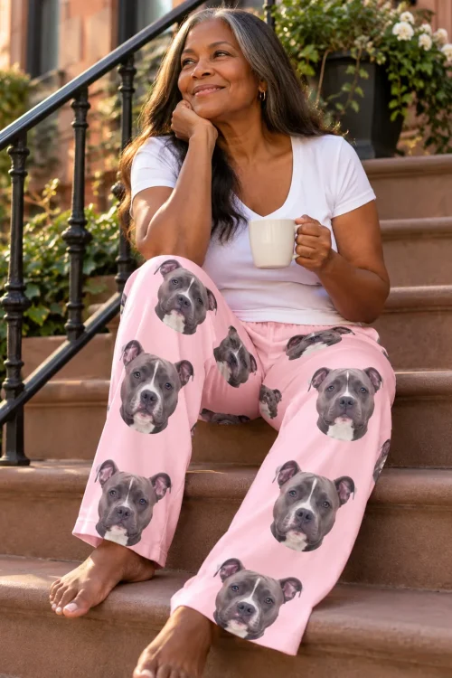 Woman sitting on brownstone steps with a mug, smiling in blush pink pittie pajama pants