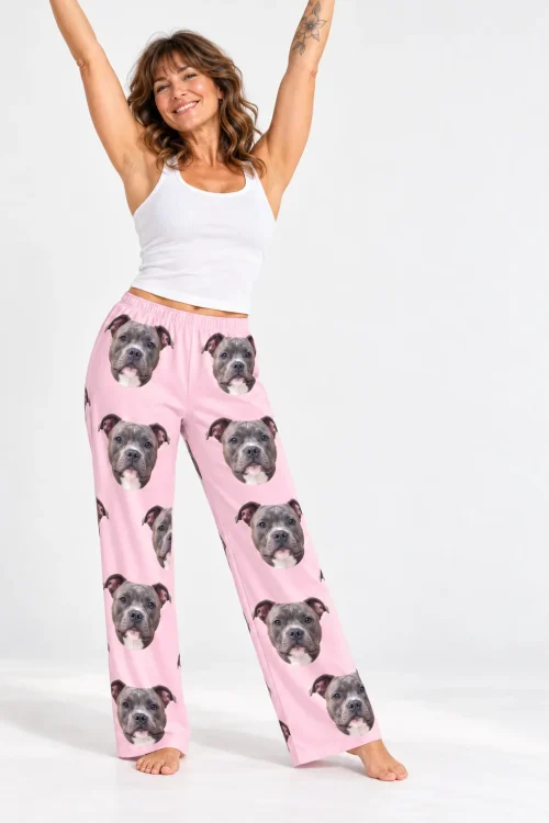 Smiling woman with arms raised in a white tank and blush pink pittie pajamas, barefoot in a white studio