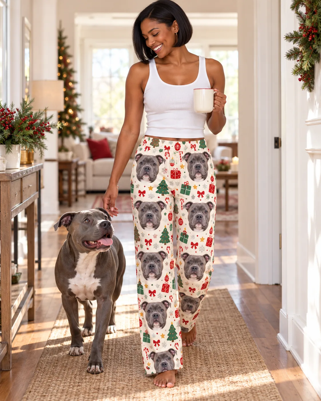 Custom Pitbull Pajama Pants for Women — christmas cream with pet | GenzOutfit Woman with a mug walking her pit bull down a festive hallway in Christmas cream pittie pajamas