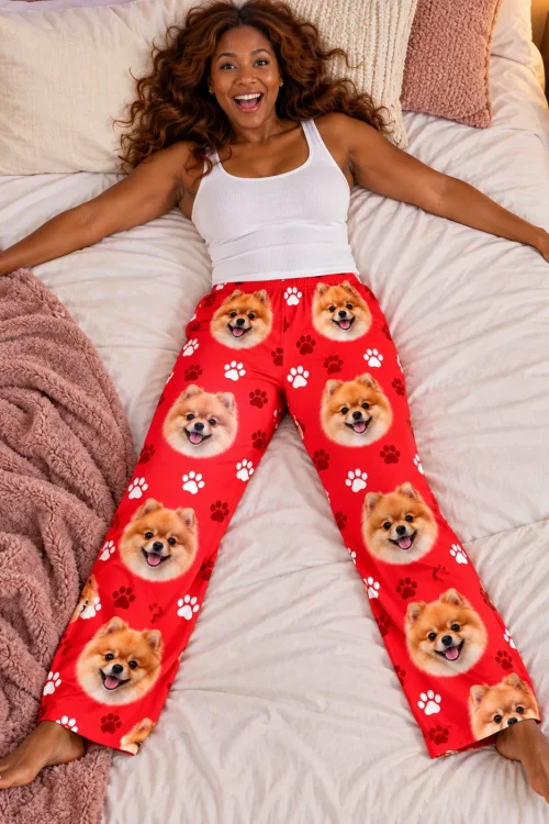 Woman lying arms wide on a bed in red paws pomeranian pajama pants, pink blanket beside her