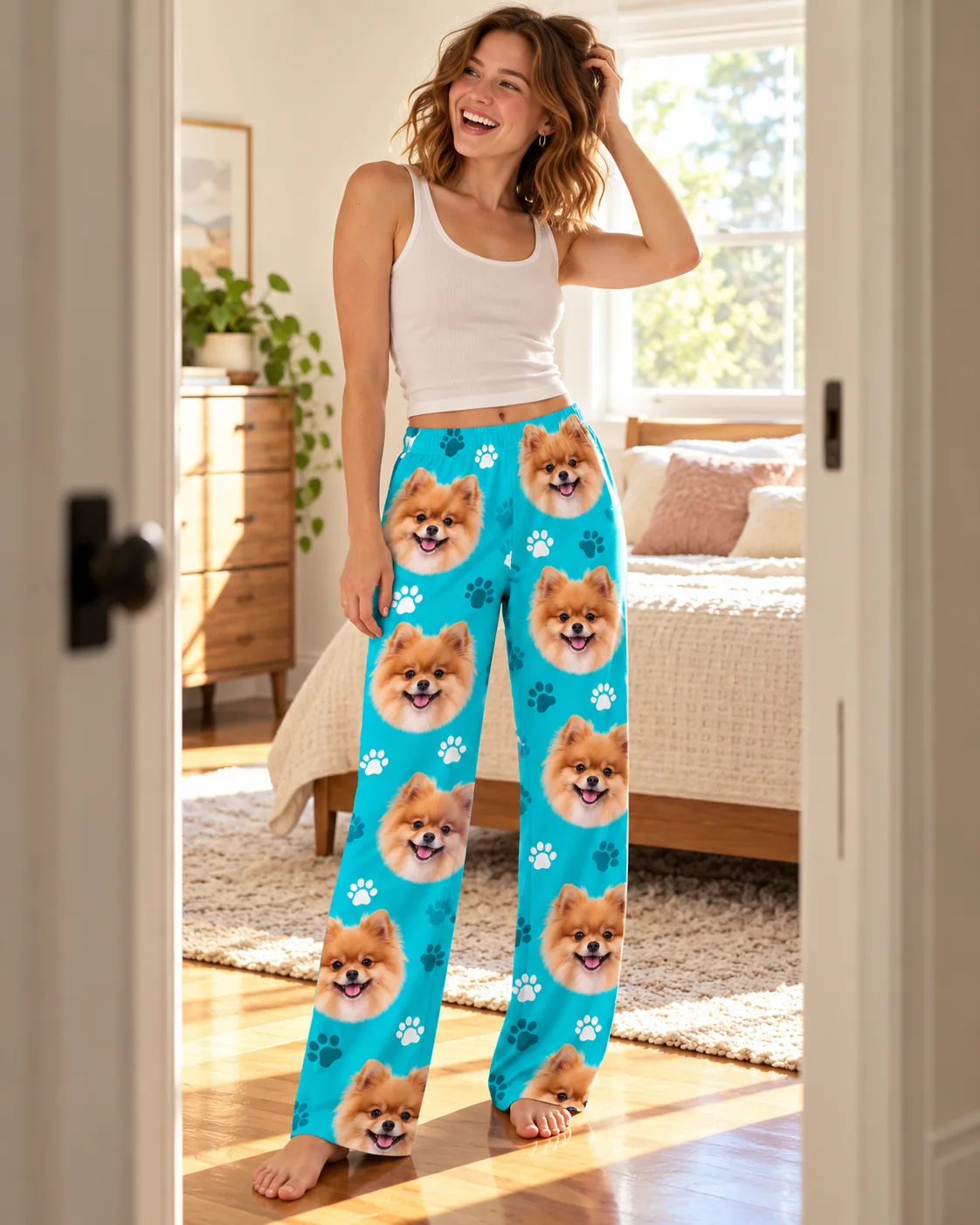 Custom Pomeranian Pajama Pants for Women — teal paws detail | GenzOutfit Smiling woman standing in a sunny bedroom doorway in teal paws pajama pants printed with pomeranian faces