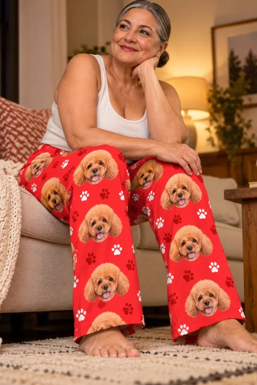 Silver-haired woman perched on a sofa arm in red paws pajama pants printed with poodle faces