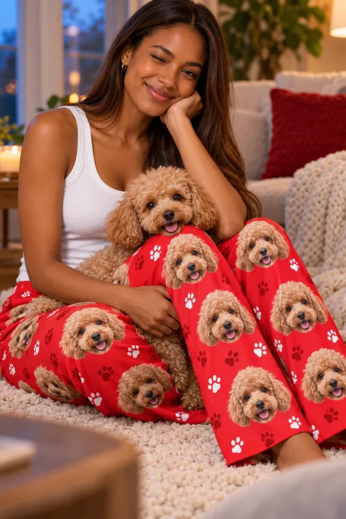 Woman winking on a shag rug, hugging her apricot poodle, in red paws poodle pajama pants