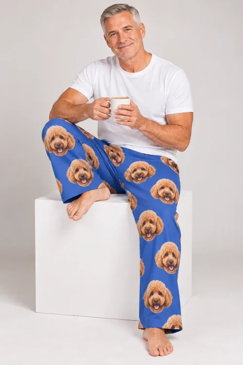Silver-haired man with a mug sitting on a white cube in royal blue poodle PJs, gray studio