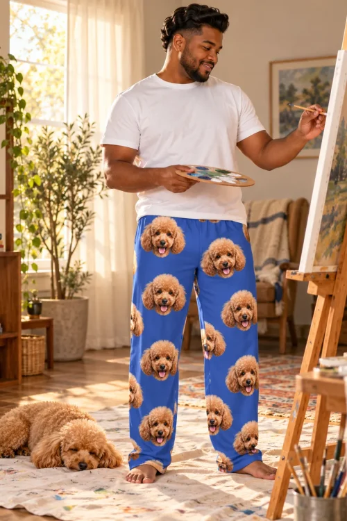 Man painting at an easel in royal blue poodle PJs while his apricot poodle naps on the rug