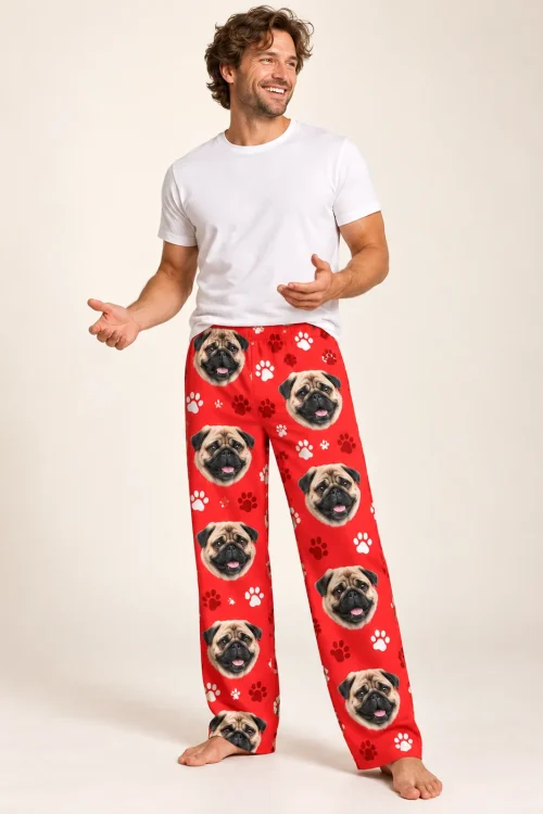 Curly-haired man in a white tee and red paws pug pajama pants, smiling barefoot in a cream studio