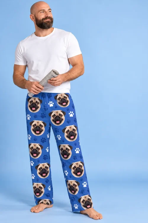 Bearded man holding a rolled newspaper in royal blue paws pajama pants printed with pug faces, blue studio