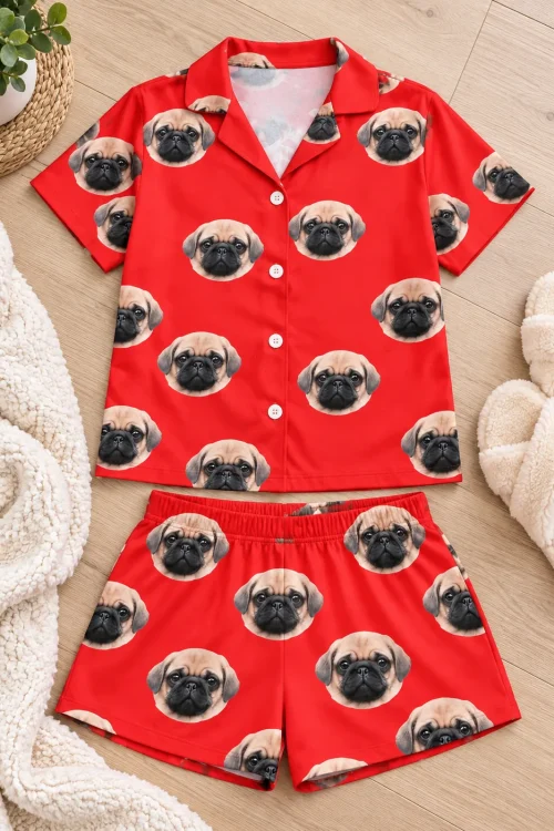 Red pajama set with pug faces laid flat on a wood floor: short-sleeve shirt and shorts beside slippers