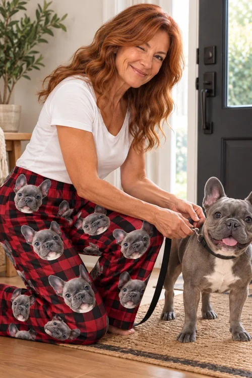 Woman kneeling to leash her French bulldog, wearing red plaid pajama pants printed with its face